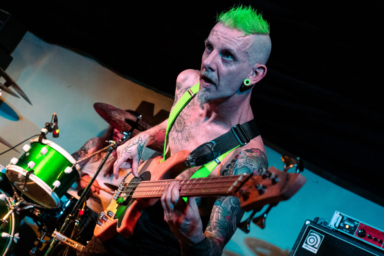 Man with green hair leaning forward with a guitar